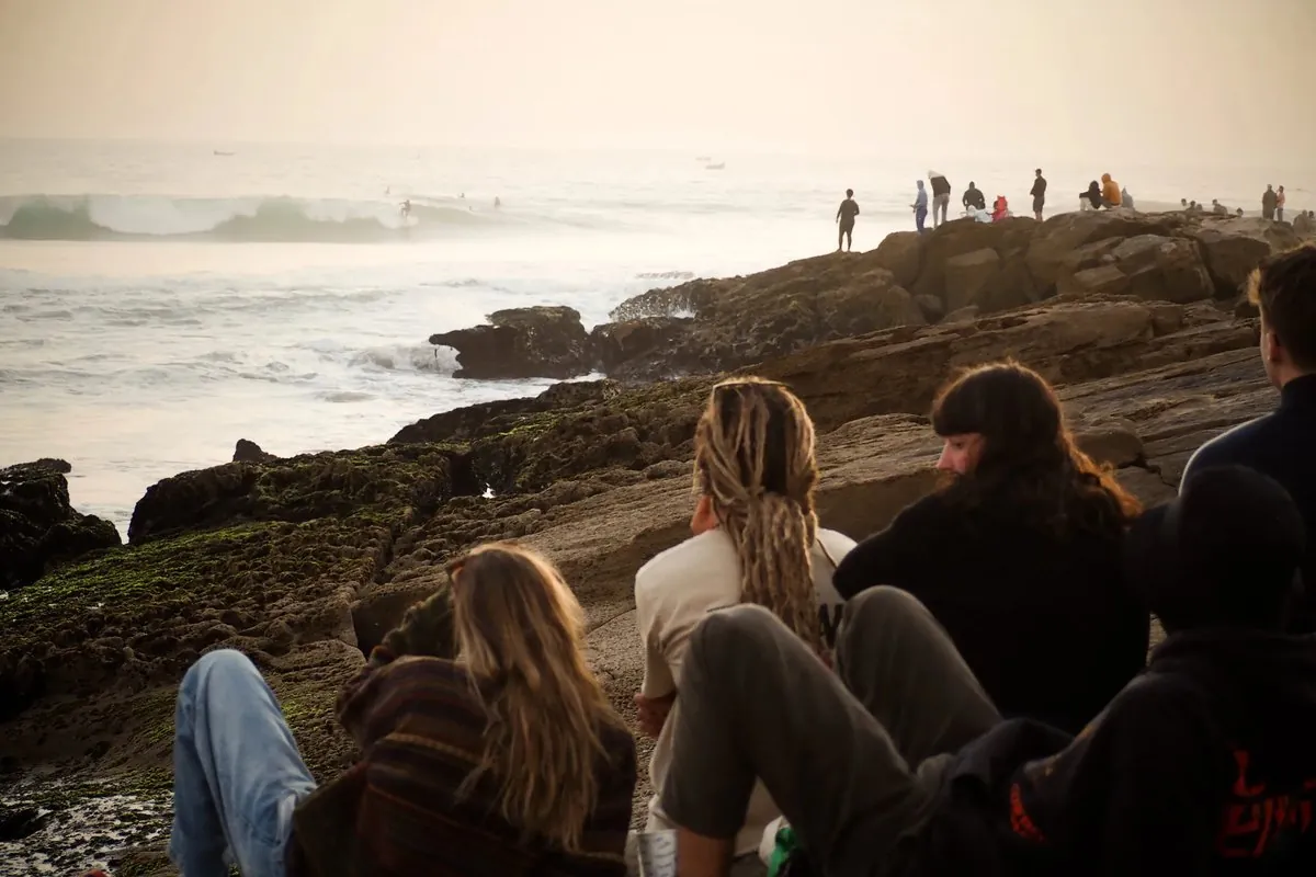 Groupe observant les vagues depuis les rochers au coucher du soleil